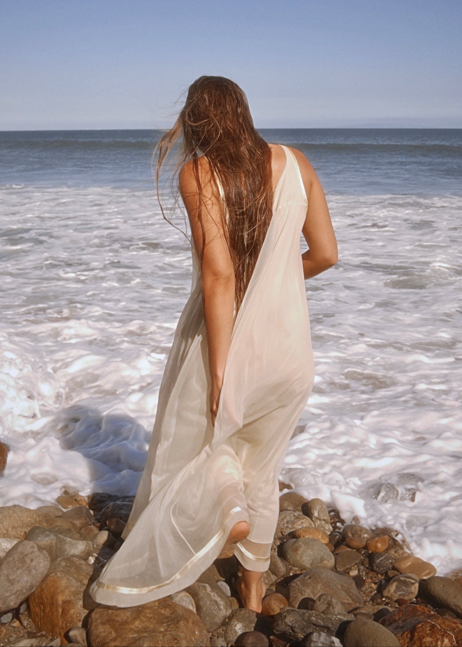 Woman in a white dress standing on rocks by the ocean